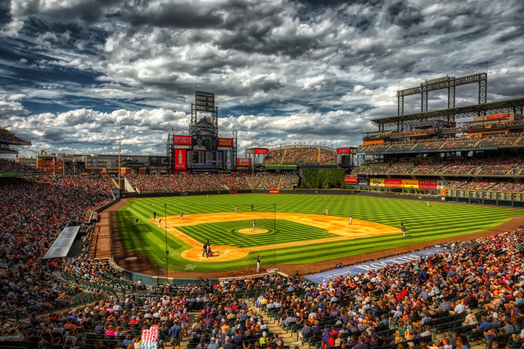 A panoramic view of a bustling baseball stadium filled with fans, featuring a vibrant green field and a cloudy sky.